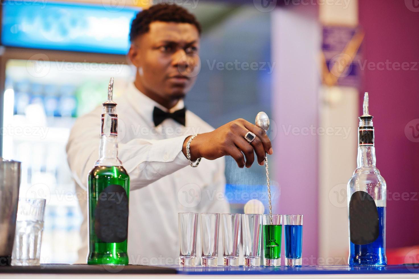Afroamerikanischer Barkeeper an der Bar, der Cocktails auf Aufnahmen macht. Zubereitung von alkoholischen Getränken. foto