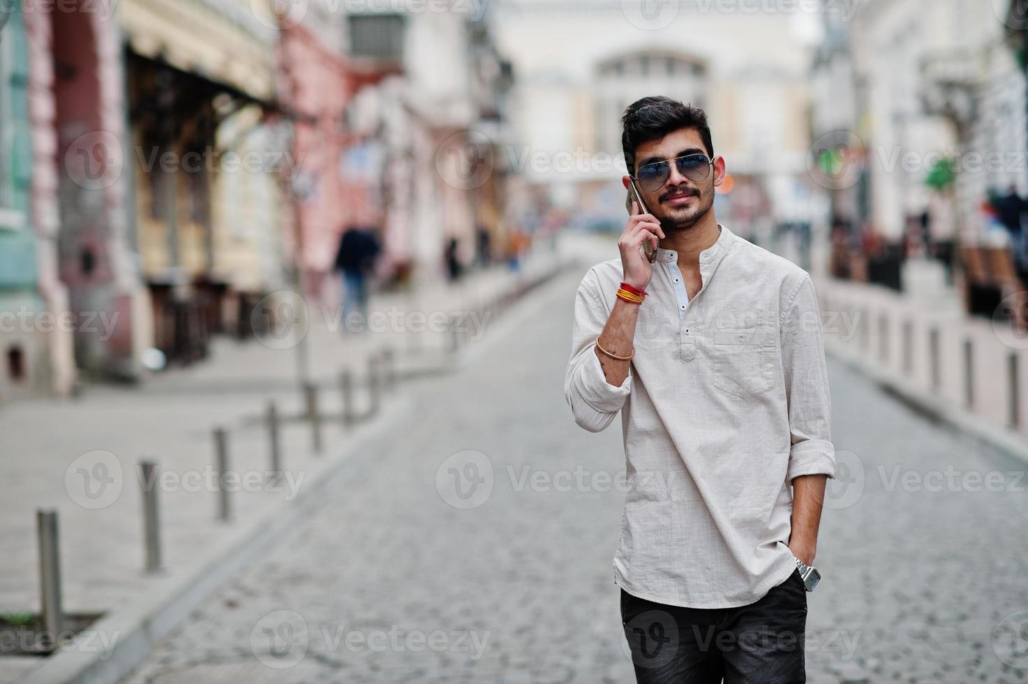 Stilvoller indischer Modellmann in Freizeitkleidung und Sonnenbrille posierte im Freien auf der Straße von Indien und telefonierte mit dem Handy. foto