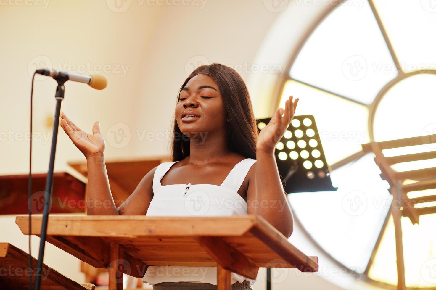 Afroamerikanerin, die in der Kirche betet. Gläubige meditieren in der Kathedrale und spirituelle Gebetszeit. Afro-Mädchen, das Gott in Refrains singt und verherrlicht. foto