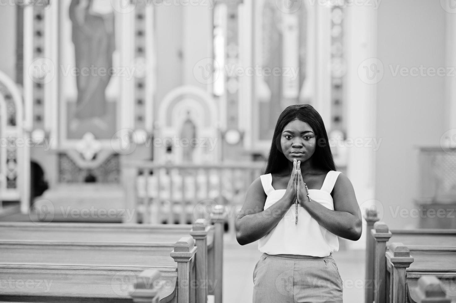 Afroamerikanerin, die in der Kirche betet. Gläubige meditieren in der Kathedrale und spirituelle Gebetszeit. Afro-Mädchen gefaltete Hände mit Rosenkranz. foto