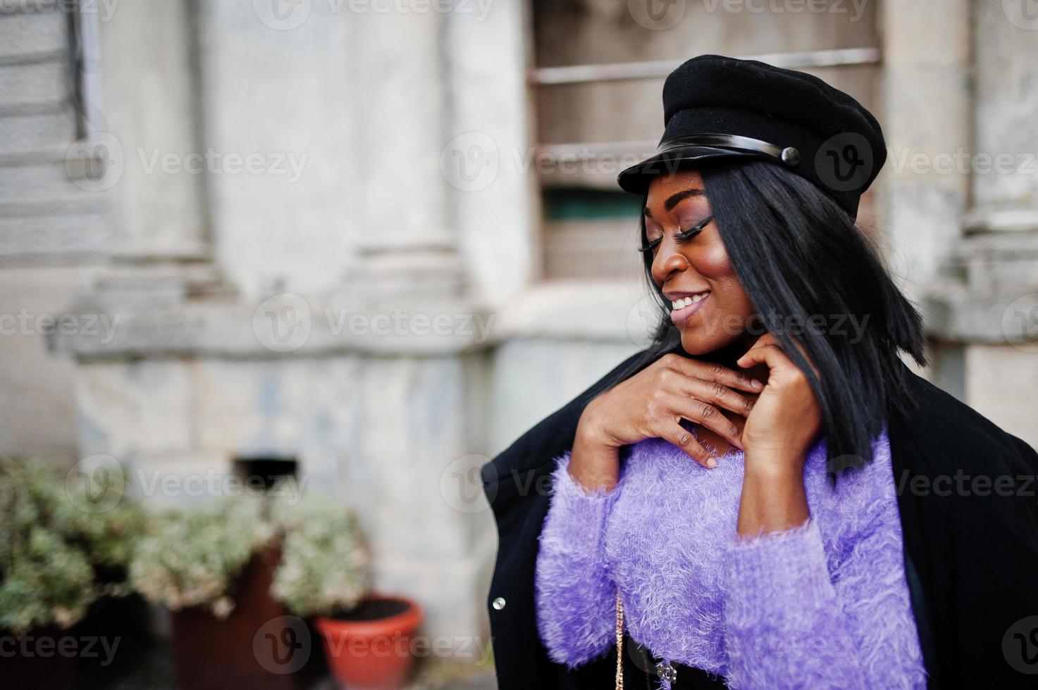 Afroamerikanerin in violettem Kleid und Mütze posierte im Freien. foto