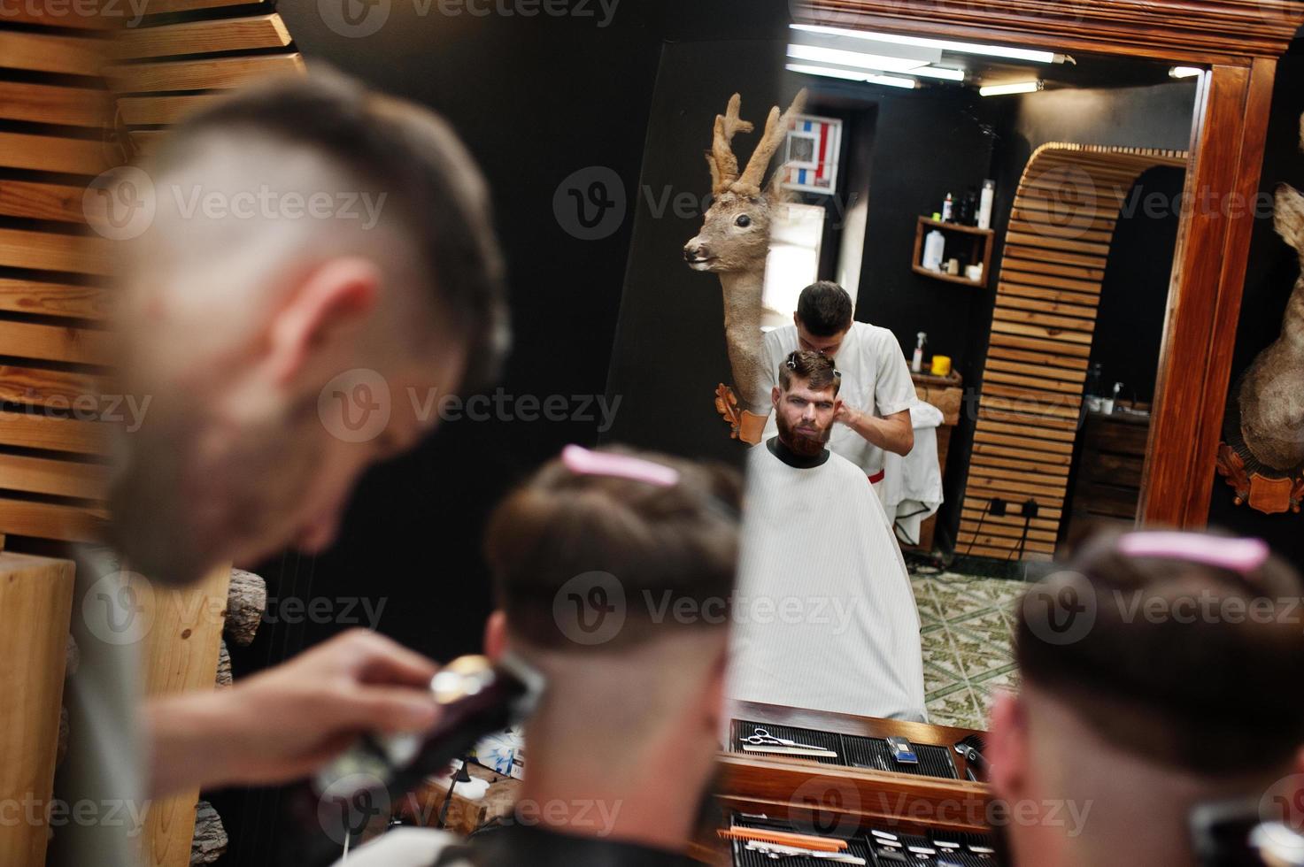 junger bärtiger mann, der vom friseur die haare schneiden lässt, während er im friseursalon auf dem stuhl sitzt. Barbier Seele. foto