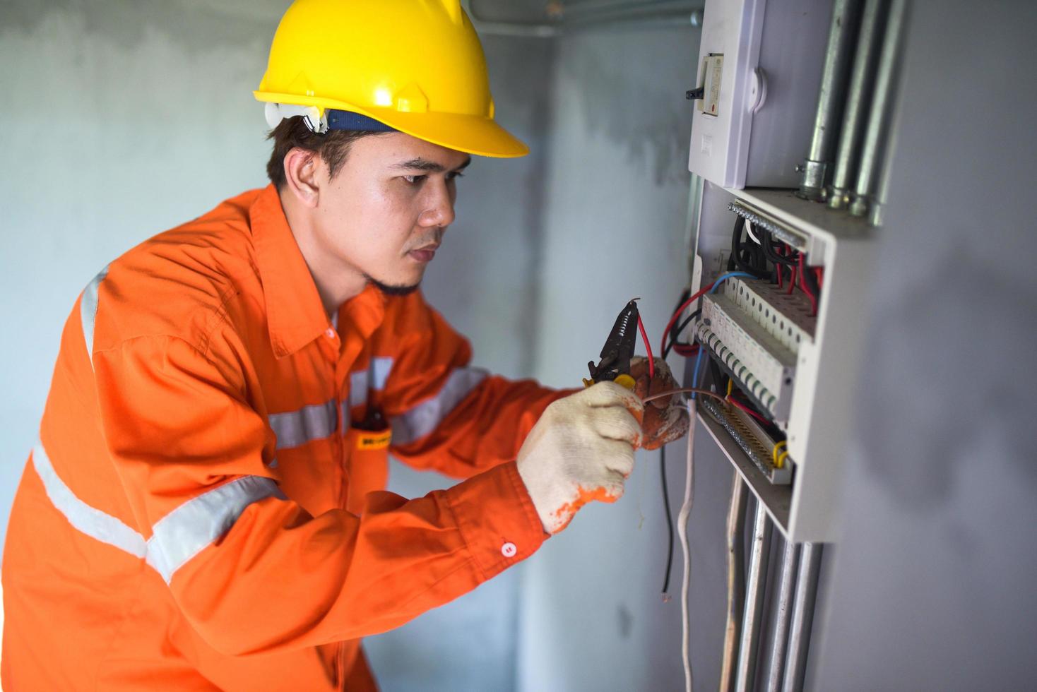 seitenansicht eines gutaussehenden asiatischen elektrikers, der einen schaltkasten mit einer zange im flur repariert. foto