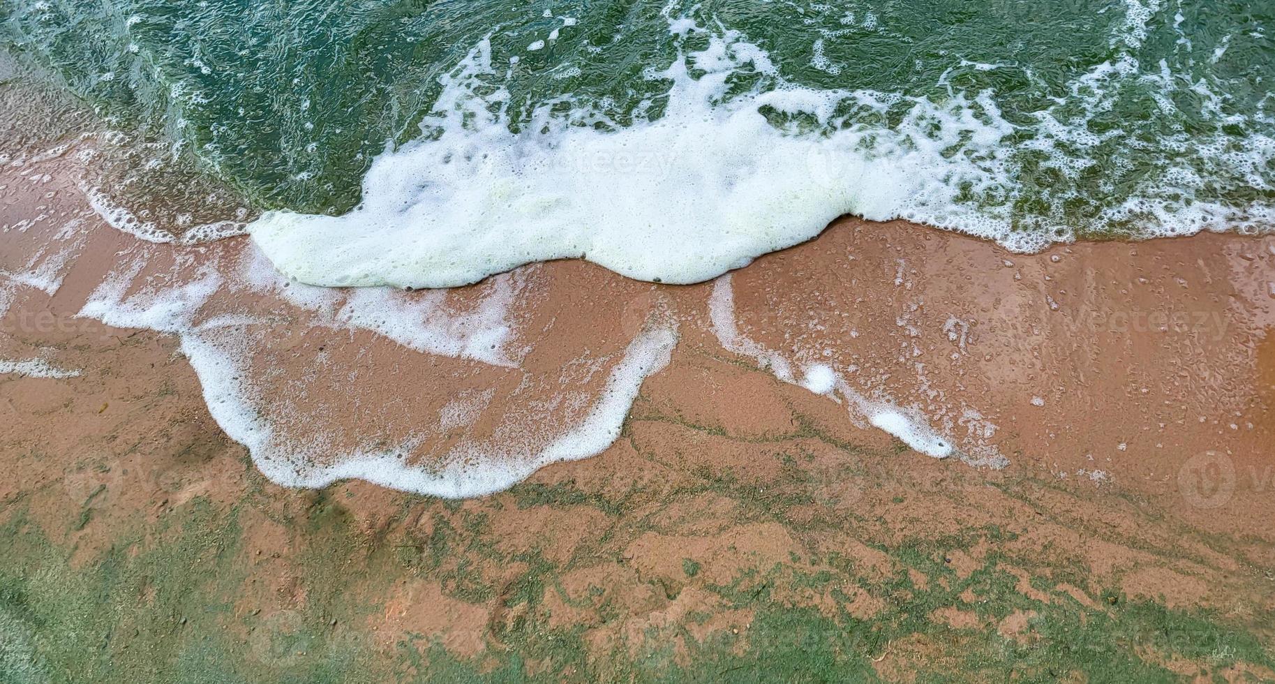 schaumwellen und sand.smaragdwellen von algen an einem windigen tag foto