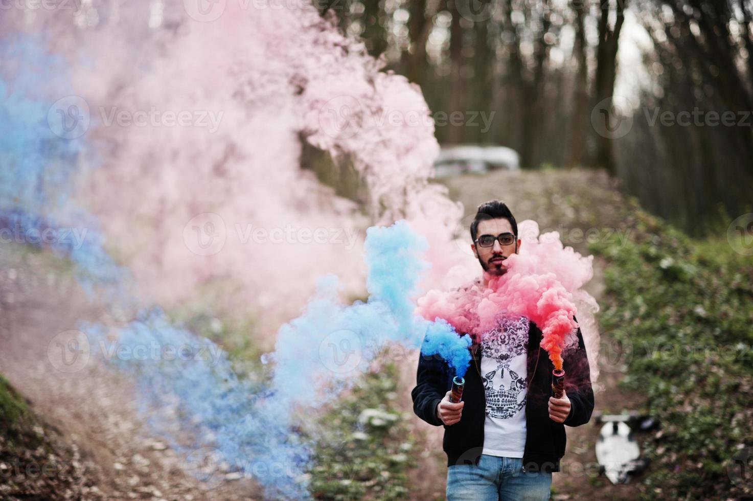 arabischer Streetstyle-Mann mit Brille hält Handfackel mit roter und blauer Rauchgranatenbombe. foto