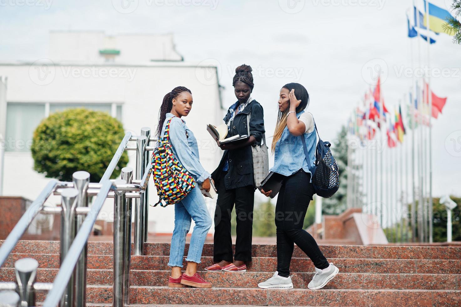 drei afrikanische studentinnen posierten mit rucksäcken und schulsachen auf dem hof der universität und schauten sich das buch an. foto