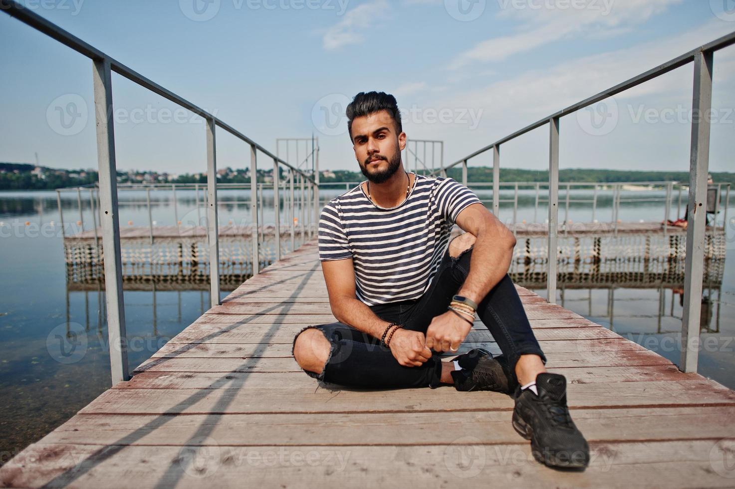 gutaussehender großer arabischer bartmannmodell im abgestreiften hemd posierte im freien am pier des sees. Modischer arabischer Typ. foto