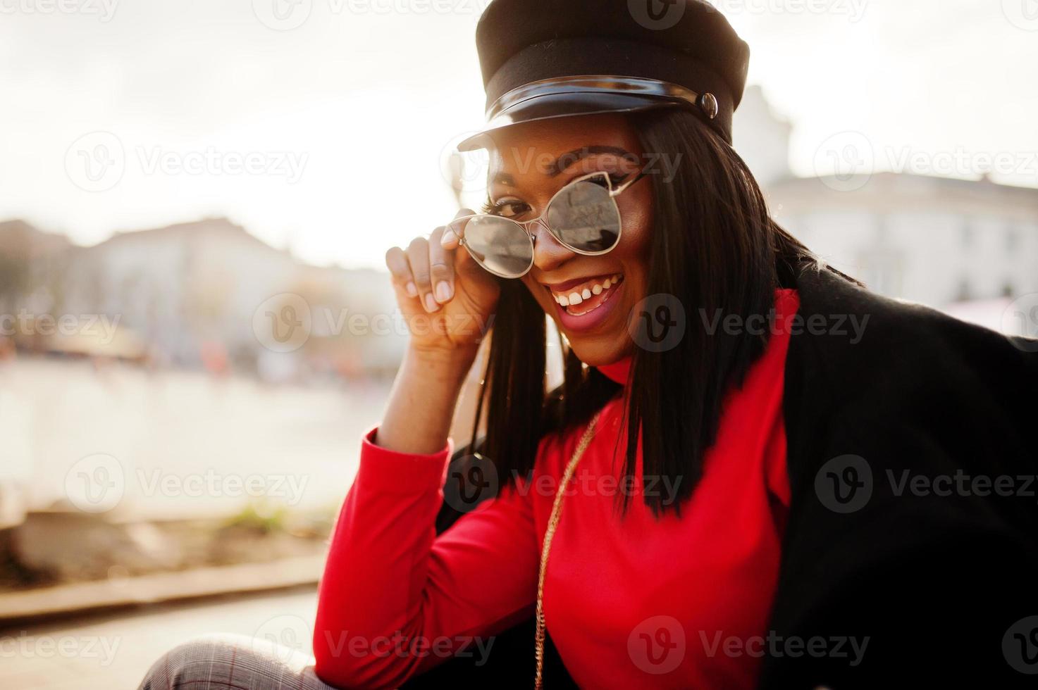 afroamerikanisches Modemädchen in Mantel und Zeitungsjungenmütze, Sonnenbrille auf der Straße gestellt. foto