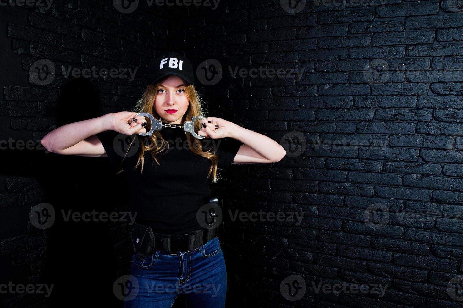 fbi-agentin in kappe und mit waffe im studio gegen dunkle backsteinmauer. foto