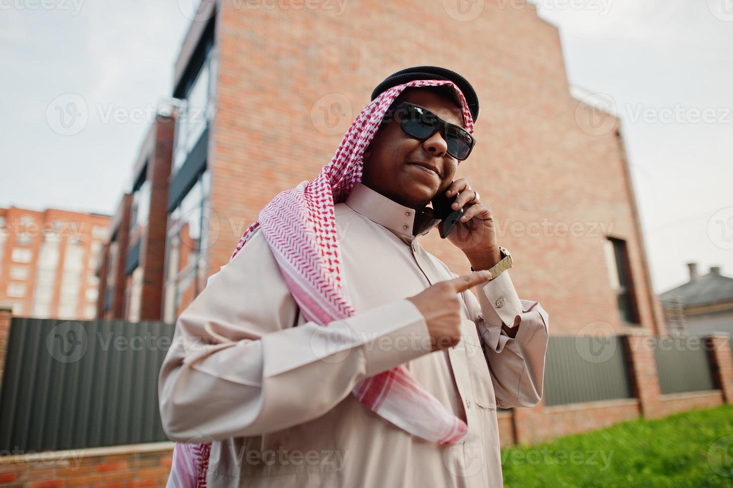 arabischer geschäftsmann aus dem nahen osten posierte auf der straße gegen modernes gebäude mit sonnenbrille und sprach mit dem handy. foto