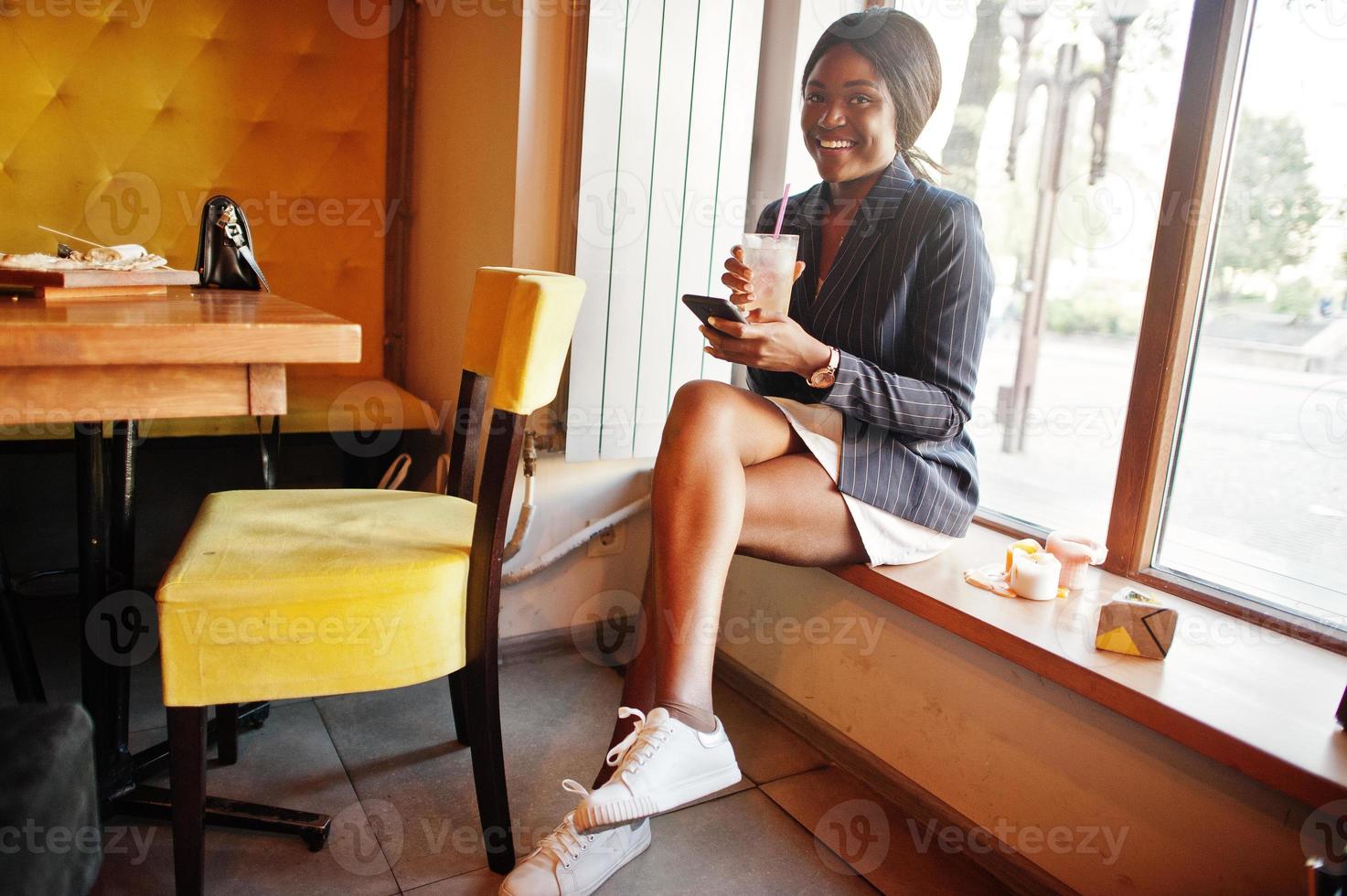 Afroamerikanische Geschäftsfrau trinkt Cocktaillimonade im Café. Schwarzes Mädchen, das sich mit dem Handy ausruht. foto