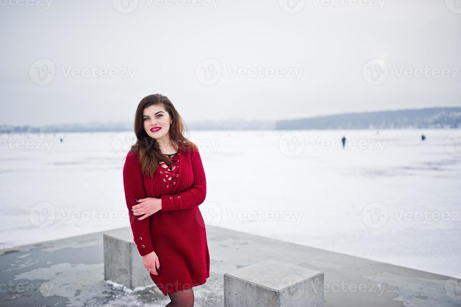 Brünette plus Größenmodell bei Rot gegen zugefrorenen See am Wintertag. foto