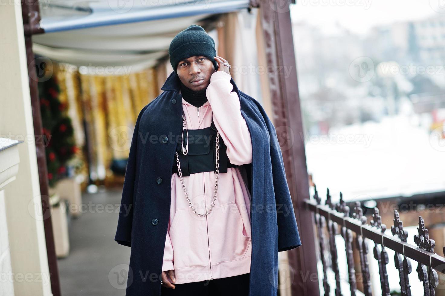 stilvoller afroamerikanischer mann im urbanen stil in schwarzem mantel und hut, rosa hoodie posierte am wintertag. foto