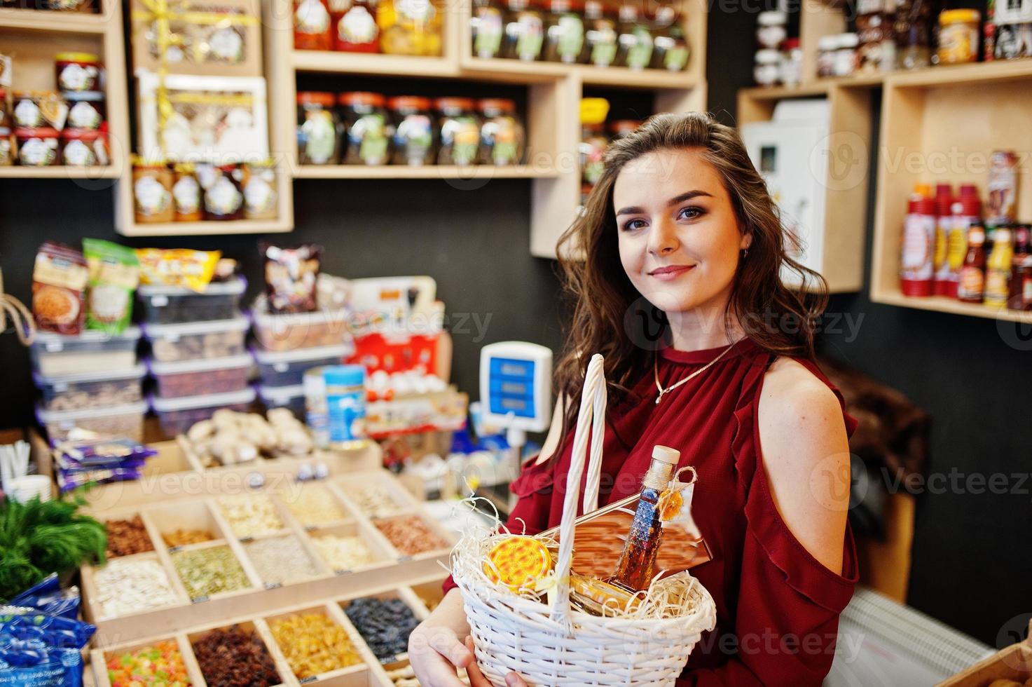 Mädchen in Rot, das verschiedene Produkte auf Korb im Feinkostgeschäft hält. foto