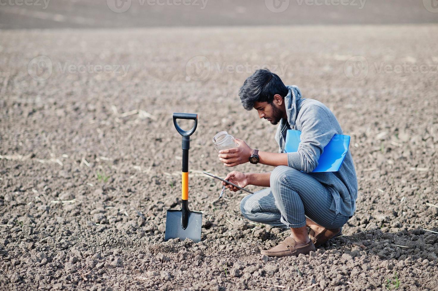 Südasiatischer agronomischer Bauer mit Schaufel, der schwarzen Boden inspiziert. landwirtschaftliches Produktionskonzept. foto