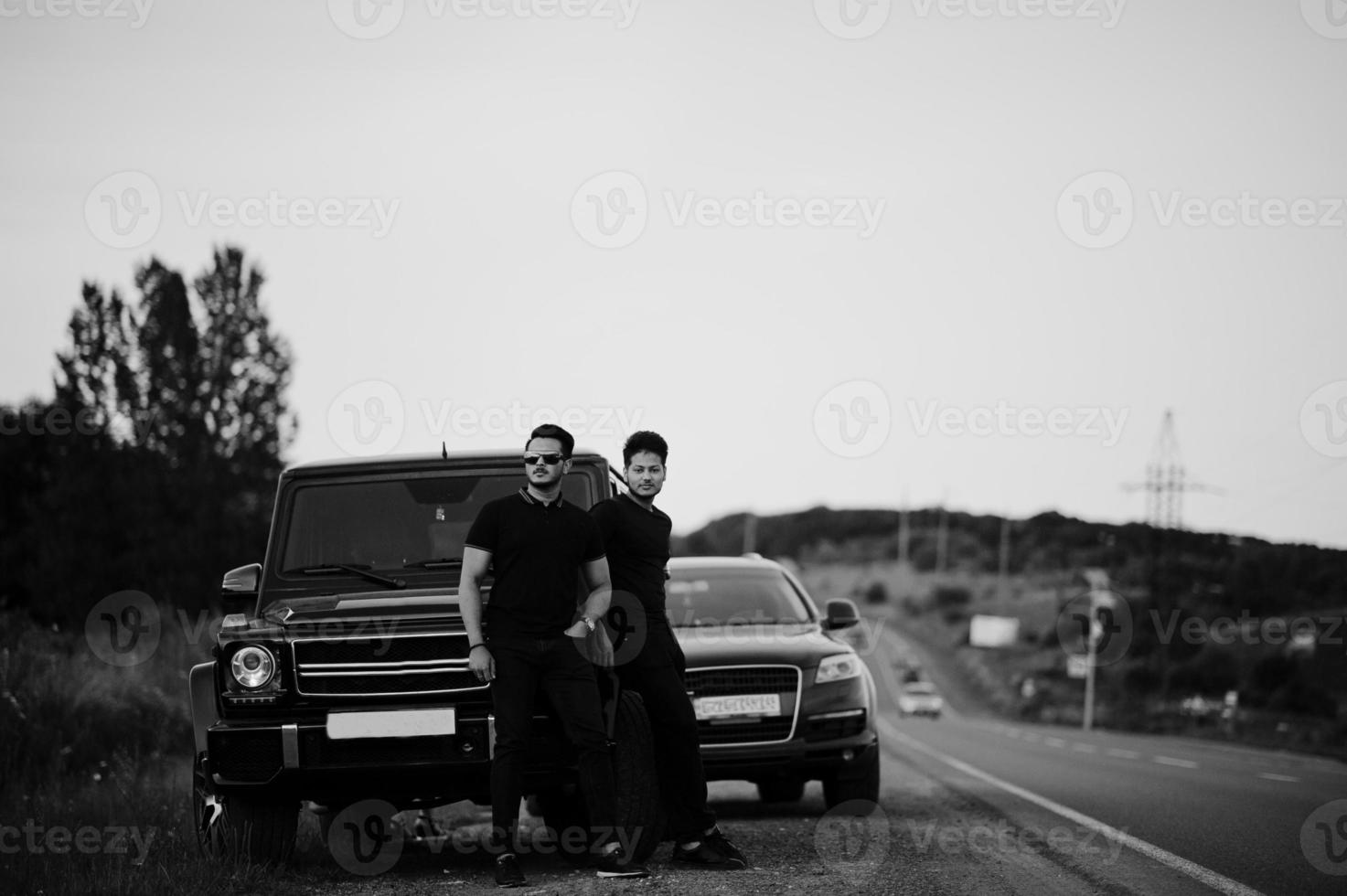 zwei asiatische brüder tragen alles schwarz und posieren in der nähe von suv-autos. foto