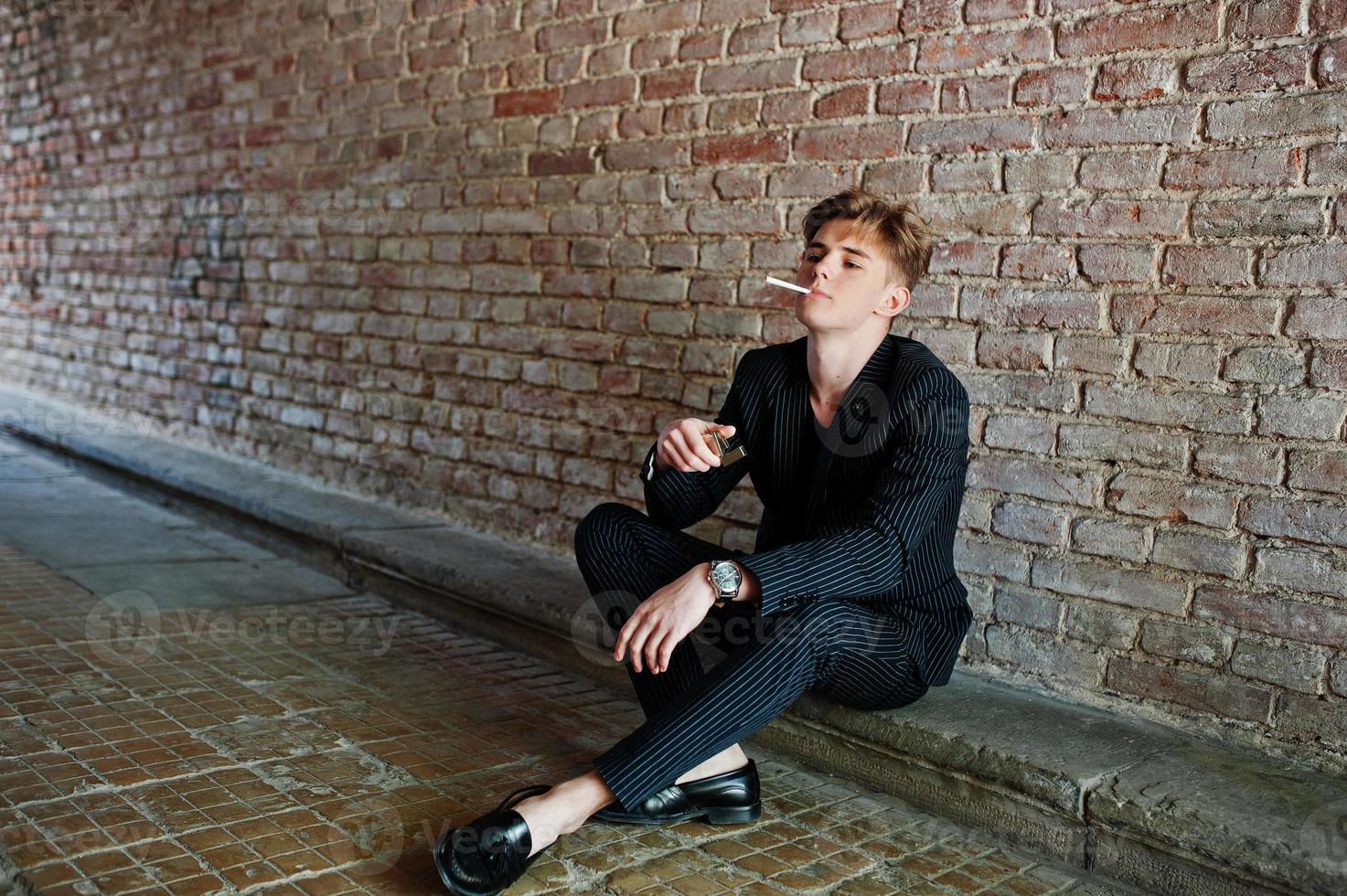 junger macho-junge trägt eine schwarze stylische jacke, die auf straßen zigarette raucht. foto