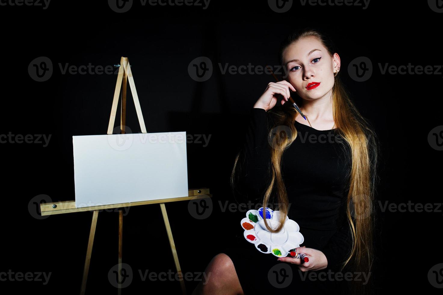 schöne Künstlerin Malerin mit Pinsel und Ölleinwand posiert im Studio isoliert auf schwarz. foto