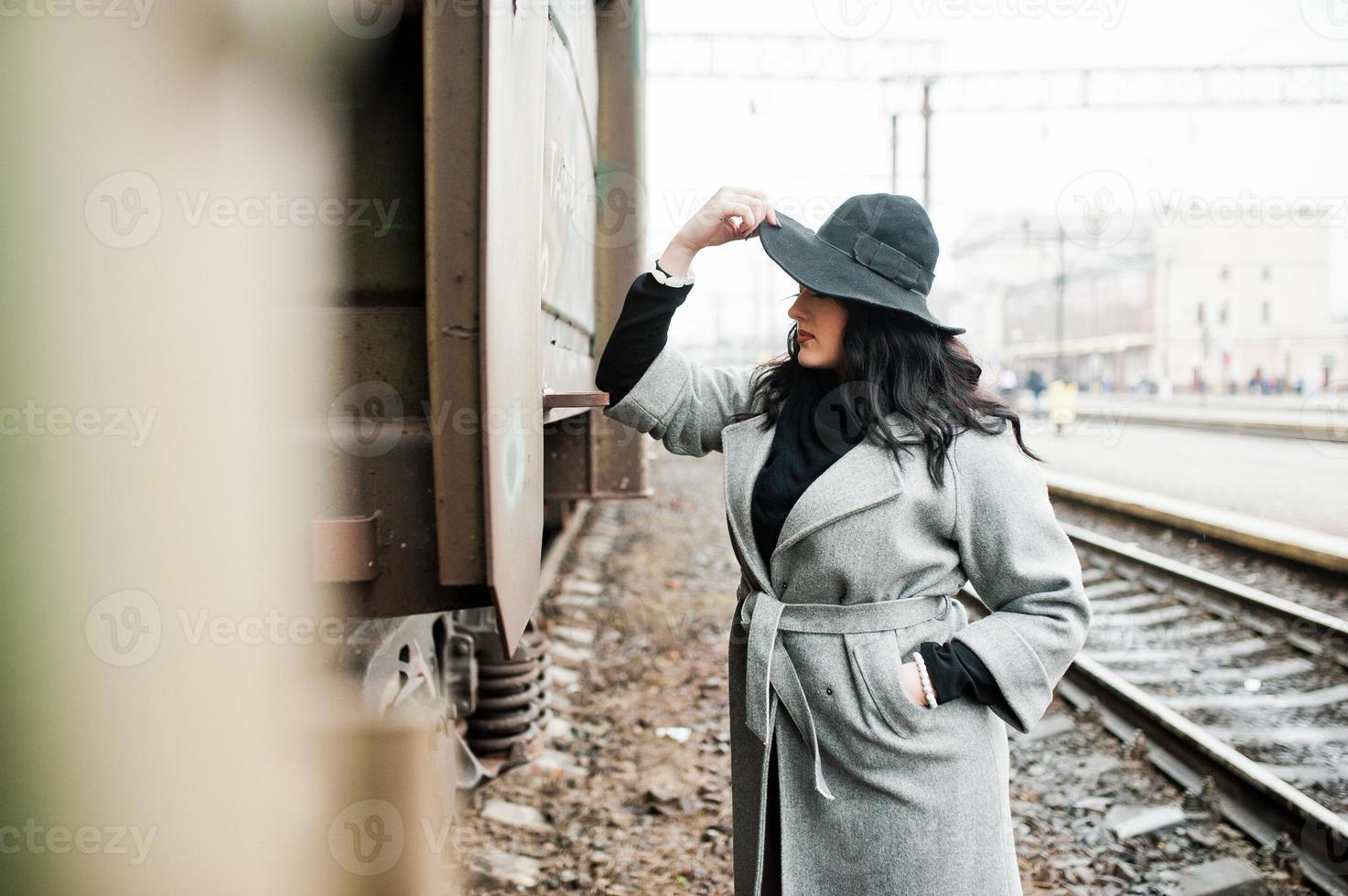 Brünettes Mädchen im grauen Mantel mit Hut im Bahnhof. foto