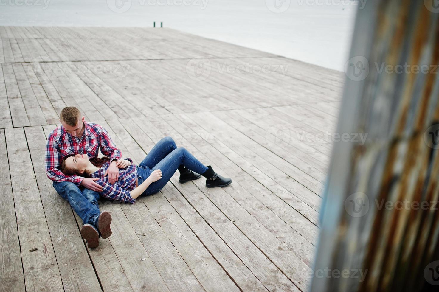 Stilvolles Paar trägt ein kariertes Hemd, das verliebt zusammen auf dem Pier sitzt. foto