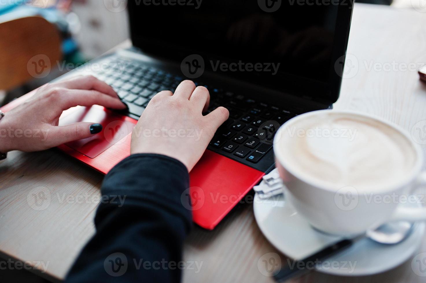 Nahaufnahme der Hände eines Mädchens, das mit einem roten Laptop mit einer Tasse Cappuccino arbeitet. foto