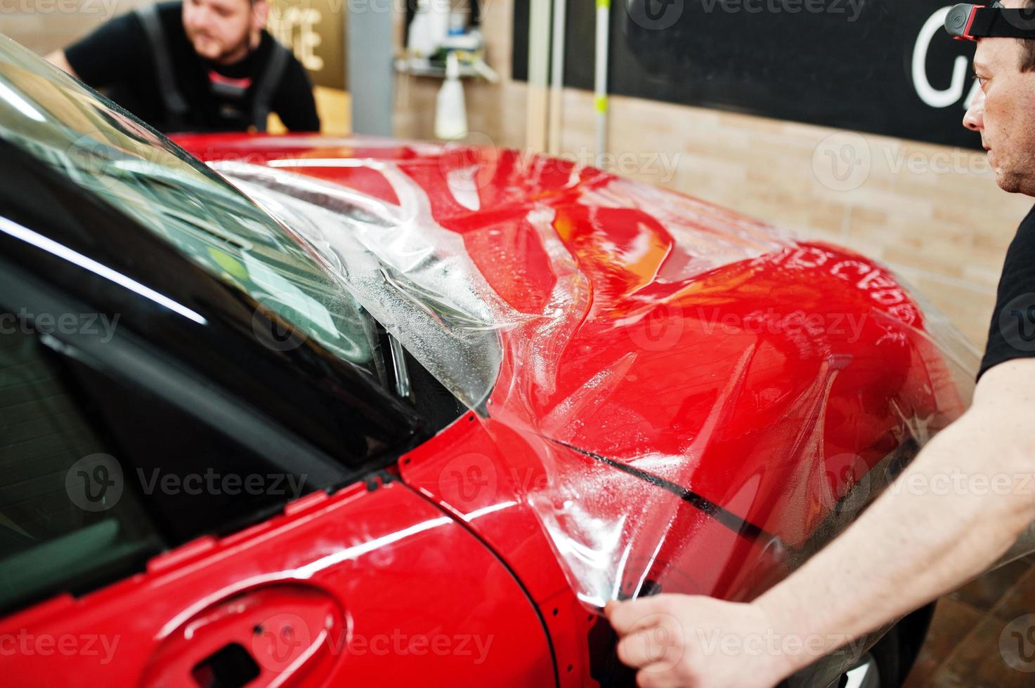 Der Autoservice-Mitarbeiter legte in der Detaillierungsfahrzeugwerkstatt eine Anti-Kies-Folie auf eine rote Karosserie. Autoschutz mit Spezialfolien. foto