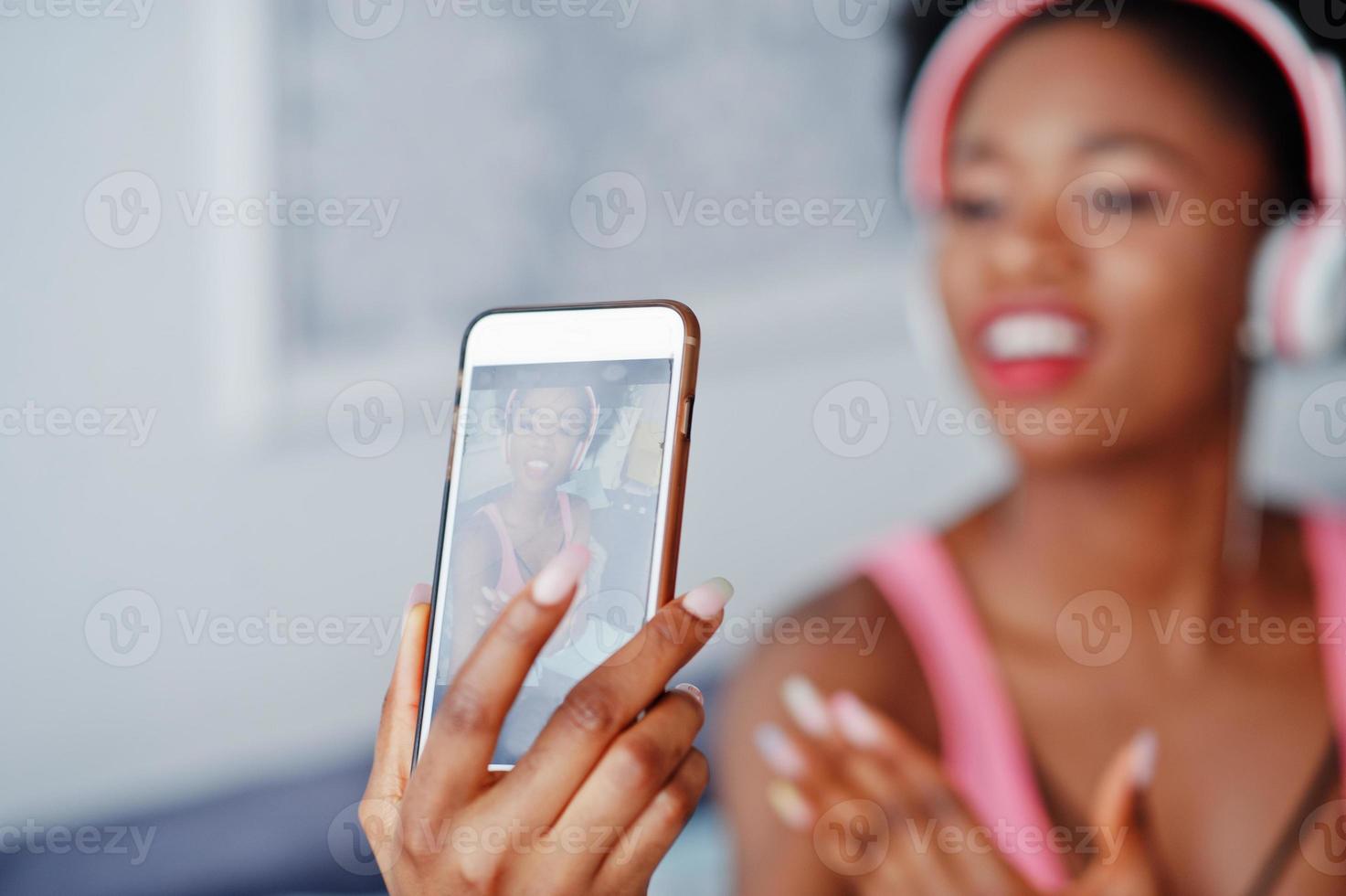 Foto der jungen afroamerikanischen Frau auf dem Bildschirm, Handy, die auf der Couch sitzt, Musik über Kopfhörer hören.