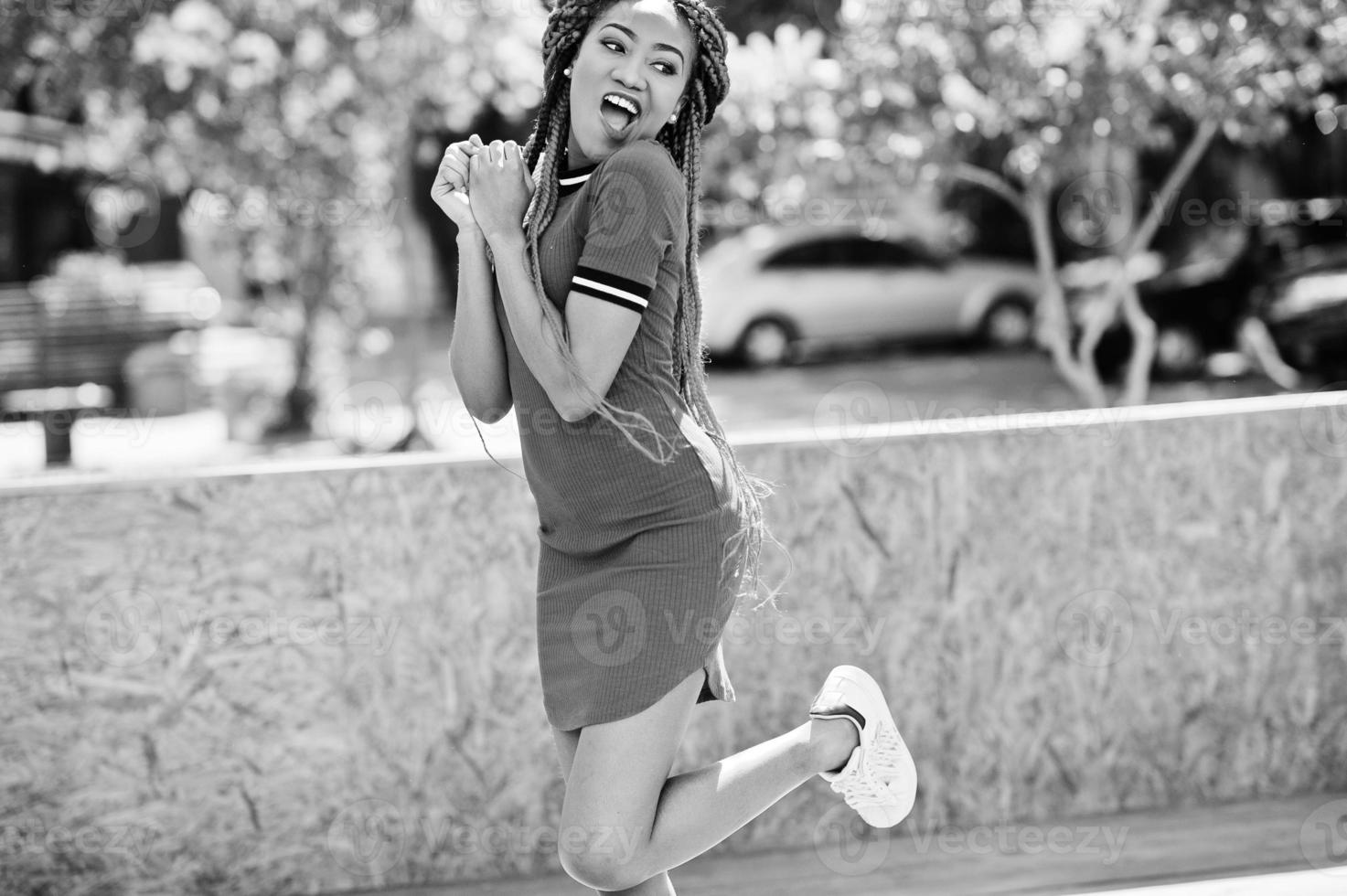 süßes und schlankes afroamerikanisches Mädchen in rotem Kleid mit Dreadlocks in Bewegung, das Spaß auf der Straße hat. stylisches schwarzes Modell. foto