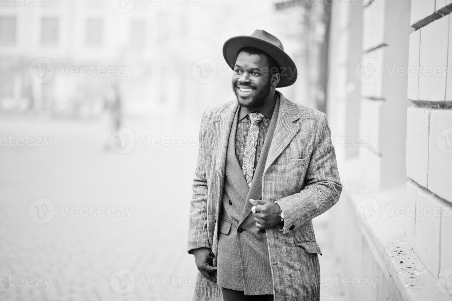 Stilvolles afroamerikanisches Mannmodell in grauem Mantel, Jackenkrawatte und rotem Hut. Schwarz-Weiß-Foto. foto