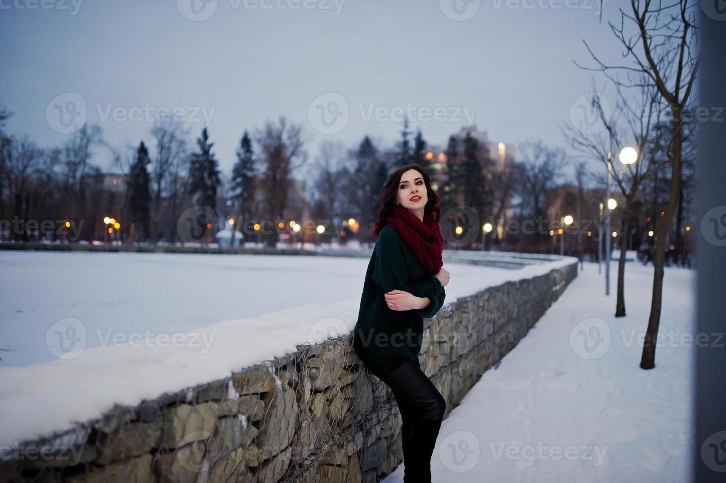 brünettes Mädchen in grünem Pullover und rotem Schal im Freien am abendlichen Wintertag. foto