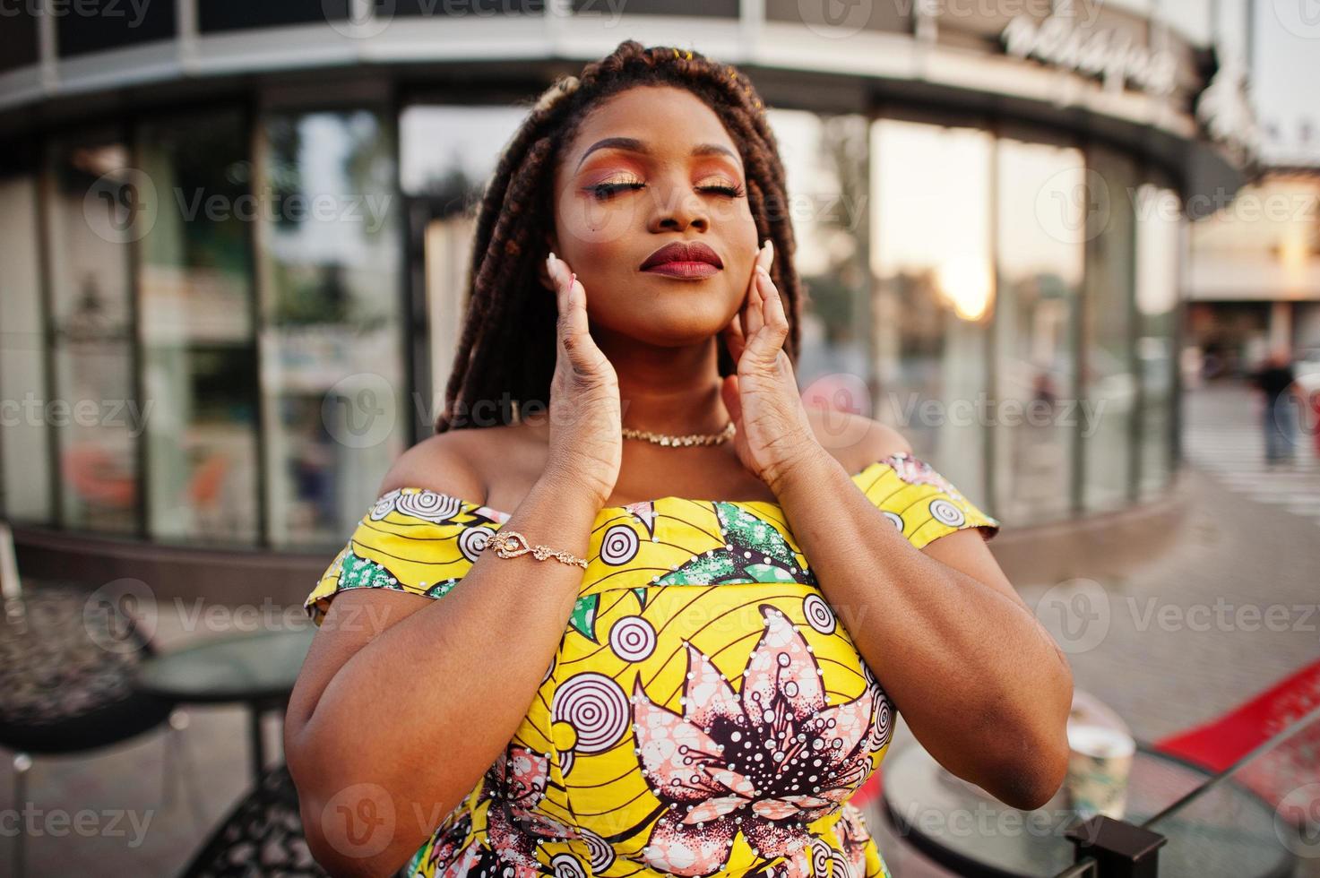 Nahaufnahme Porträt eines kleinen afroamerikanischen Mädchens mit Dreadlocks, tragen Sie ein farbiges gelbes Kleid, Gesicht mit Make-up. foto