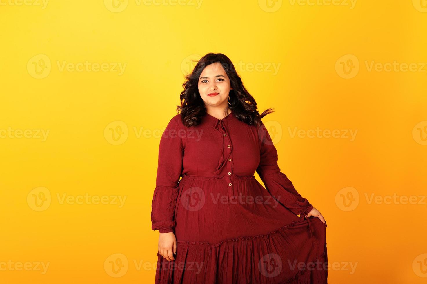 attraktive südasiatische frau in tiefrotem kleiderkleid posierte im studio auf gelbem hintergrund. foto