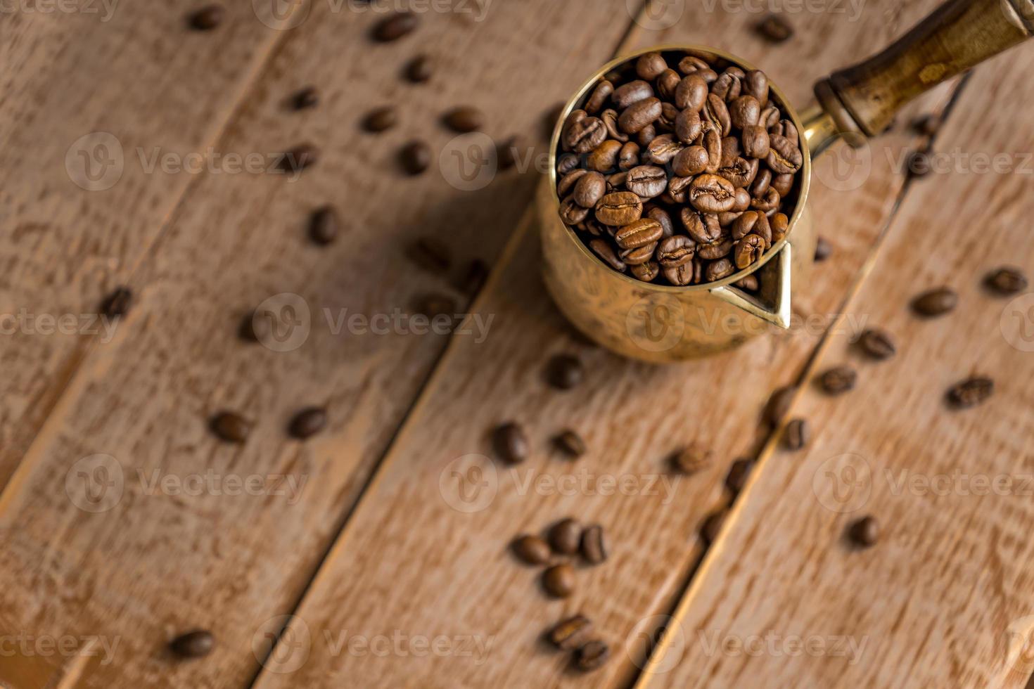 nahaufnahme von frisch gerösteten kaffeebohnen in cezve traditionelle türkische kaffeekanne auf holztisch. foto