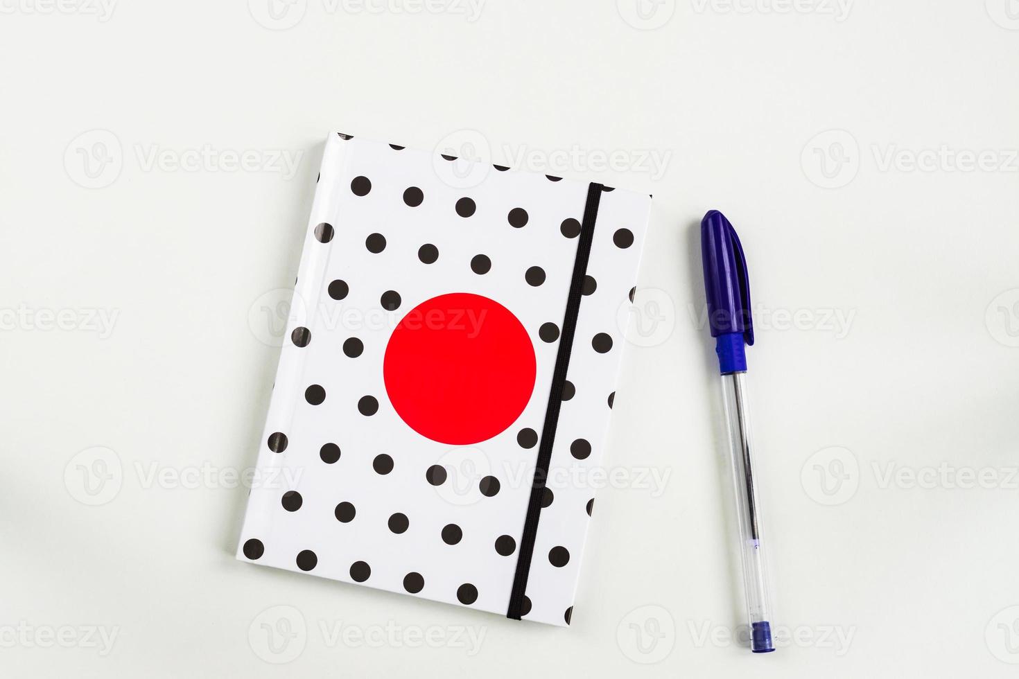 schwarz-weiß gepunktetes notizbuch mit rotem kreis auf dem cover und blauem stift auf weißem tisch. Draufsicht, minimale flache Lage foto