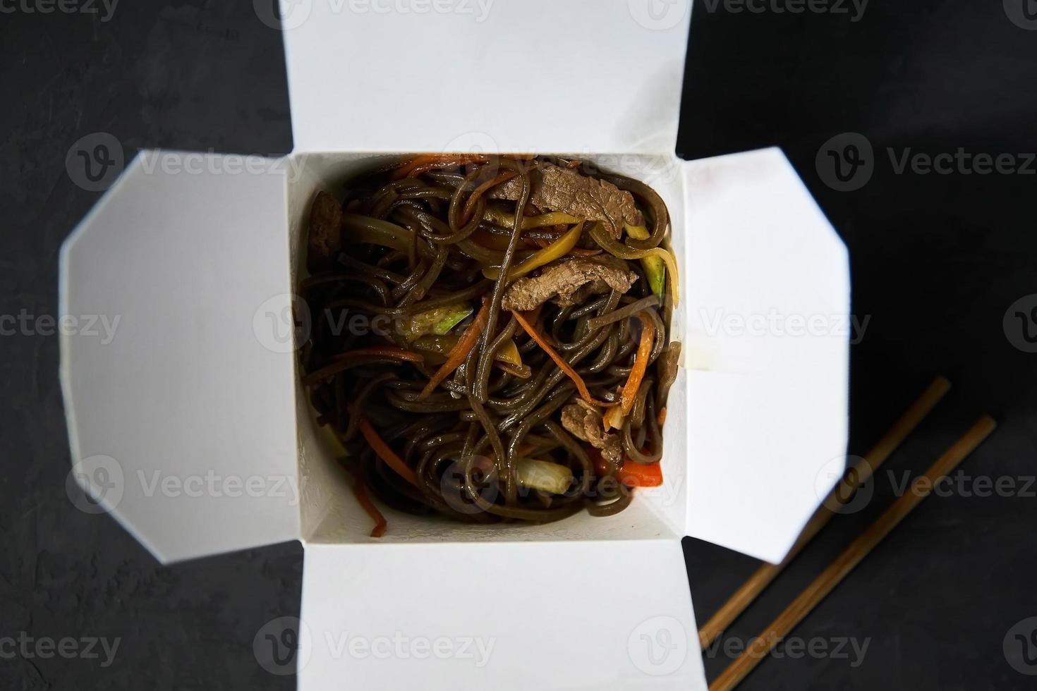 Lieferung von warmen Mittagessen in Schachteln. Soba-Nudeln mit Rindfleisch und Gemüse auf schwarzem Hintergrund foto