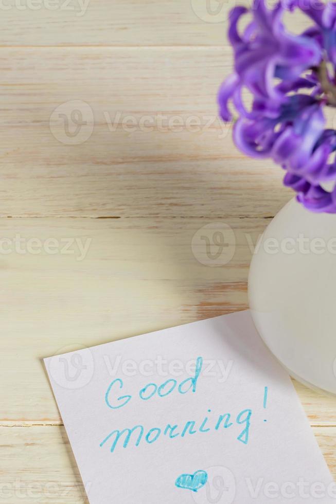 guten morgen papieretikett und lila hyazinthenblume in weißer vase auf holztisch foto