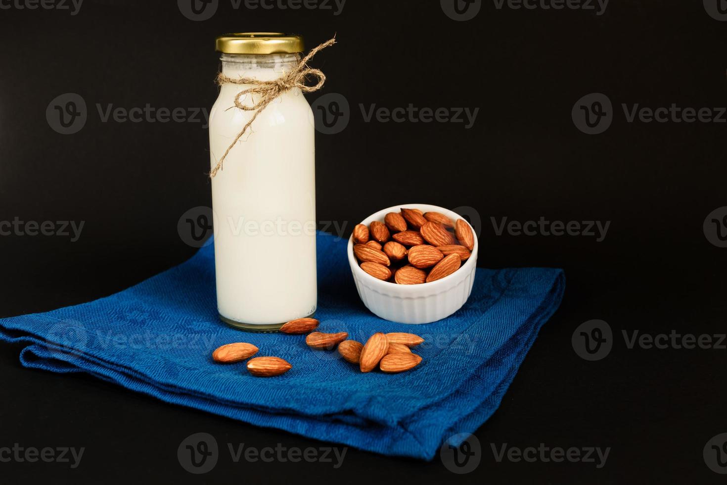 hausgemachte Mandelmilch in einer Flasche und Glas mit Nüssen in weißer Porzellanschale auf schwarzem Hintergrund. foto