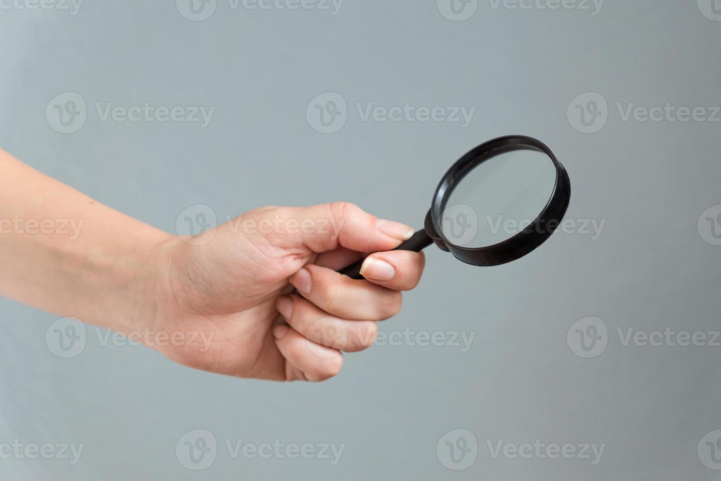 Wooman-Hand, die Lupenglas auf grauem Hintergrund hält foto