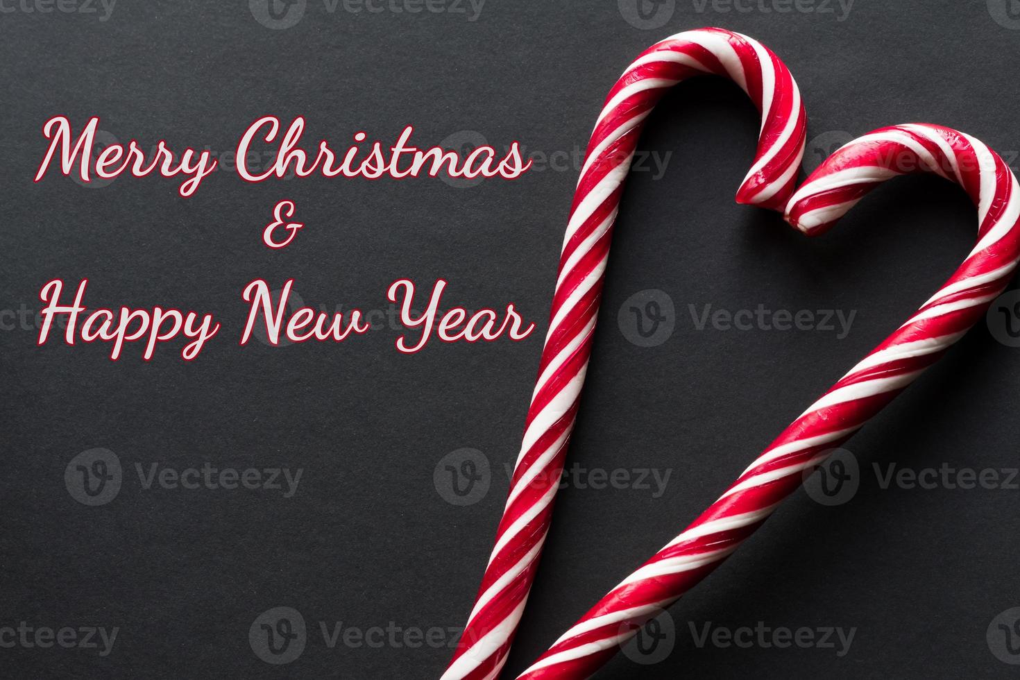 Grußkarte der frohen Weihnachten und des guten Rutsch ins Neue Jahr. Herz aus Zuckerstangen auf schwarzem Hintergrund foto