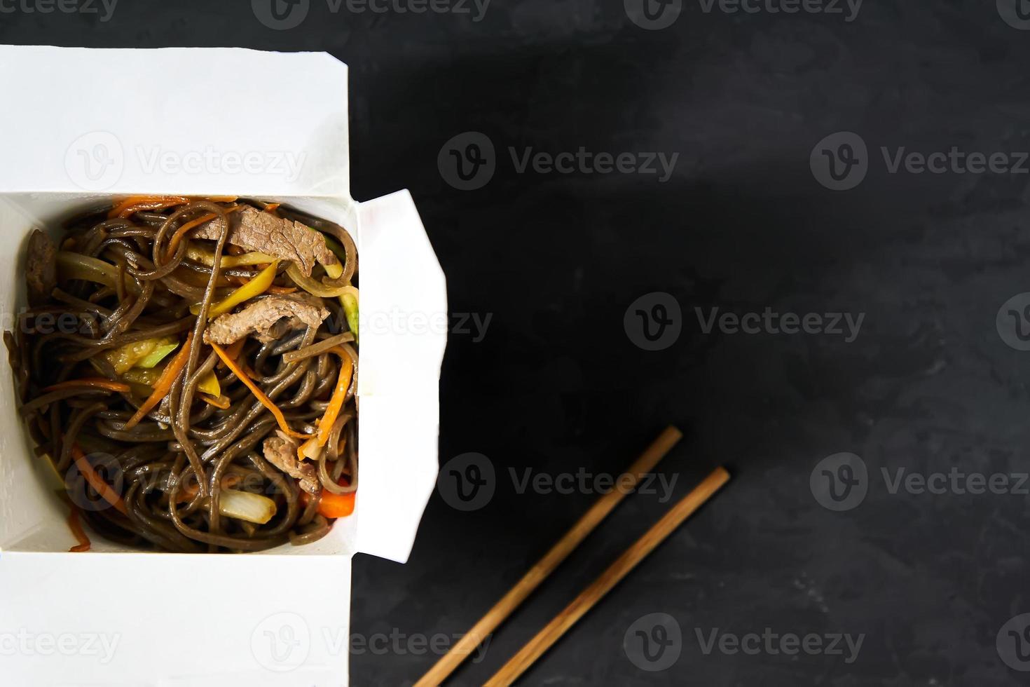 Lieferung von warmen Mittagessen in Schachteln. Soba-Nudeln mit Rindfleisch und Gemüse auf schwarzem Hintergrund foto