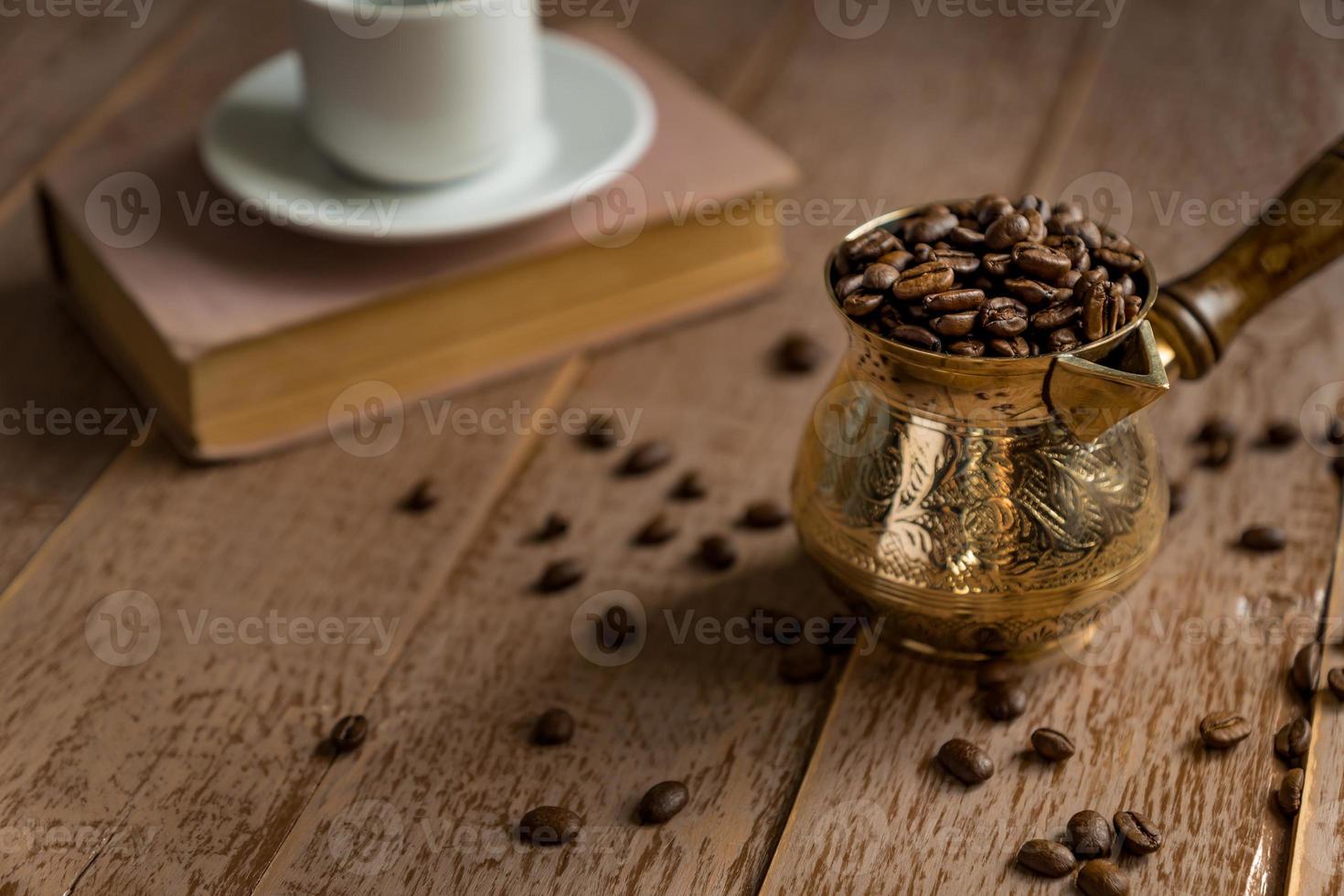 frisch geröstete kaffeebohnen in cezve traditionelle türkische kaffeekanne geschlossenes buch und tasse auf holztisch. foto