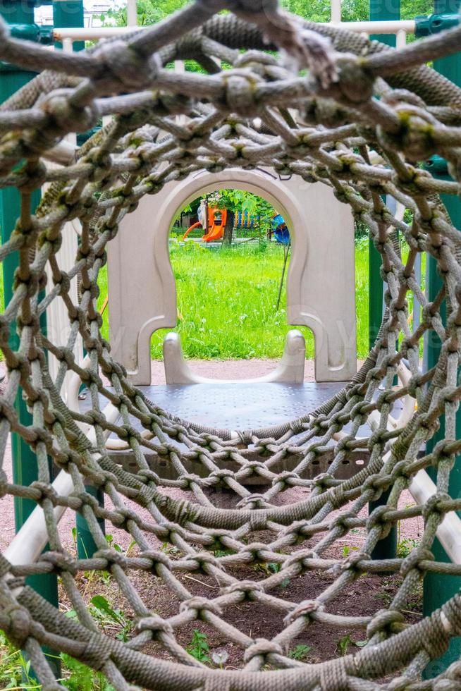 Innenansicht eines langen Seilmaschenrohrs, am Ende des Tunnels gelber Spielplatz unscharfer Hintergrund foto