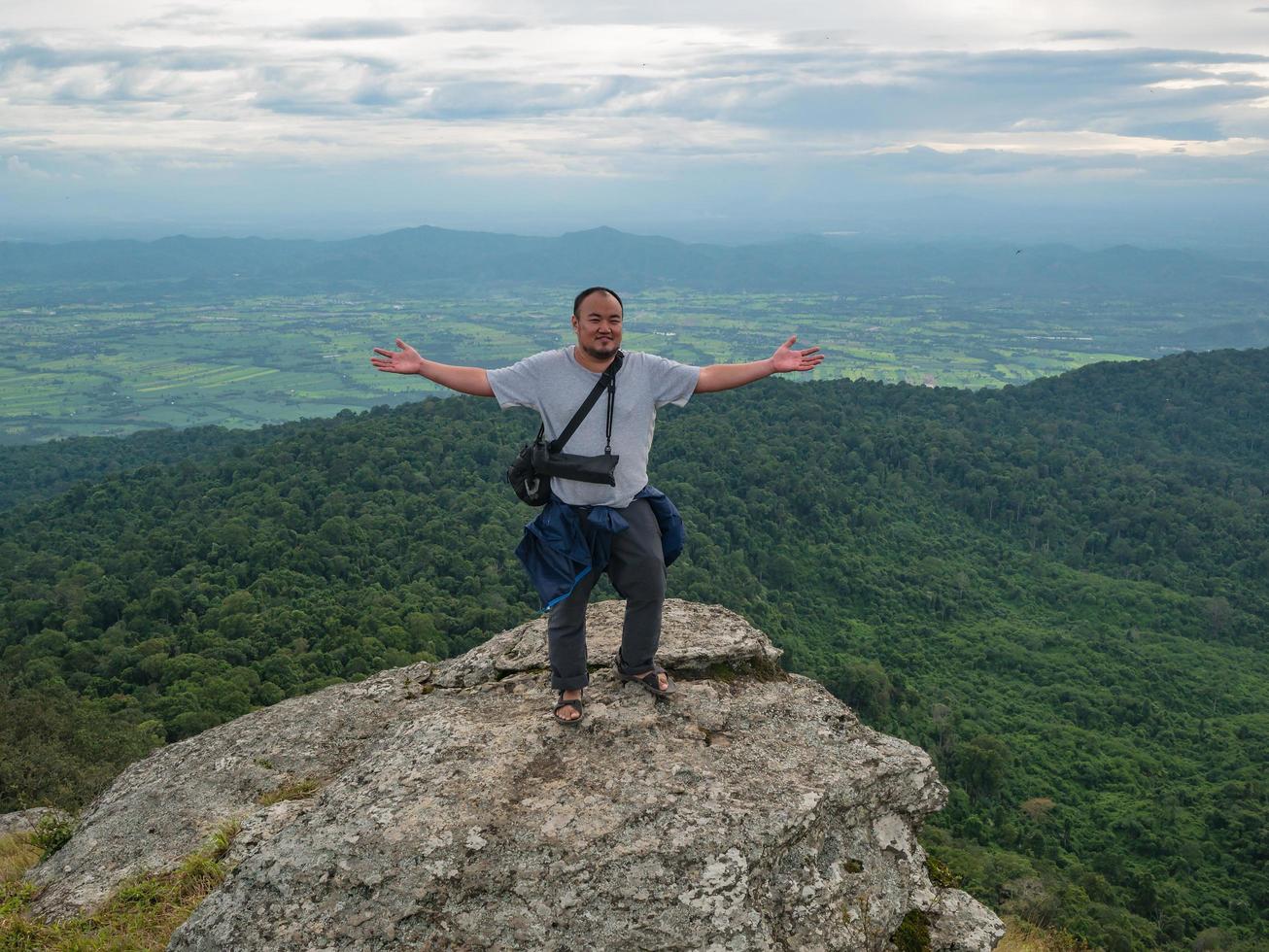 asiatischer dicker mann steht auf felsiger klippe und trekking auf khao luang berg im ramkhamhaeng nationalpark, provinz sukhothai thailand foto