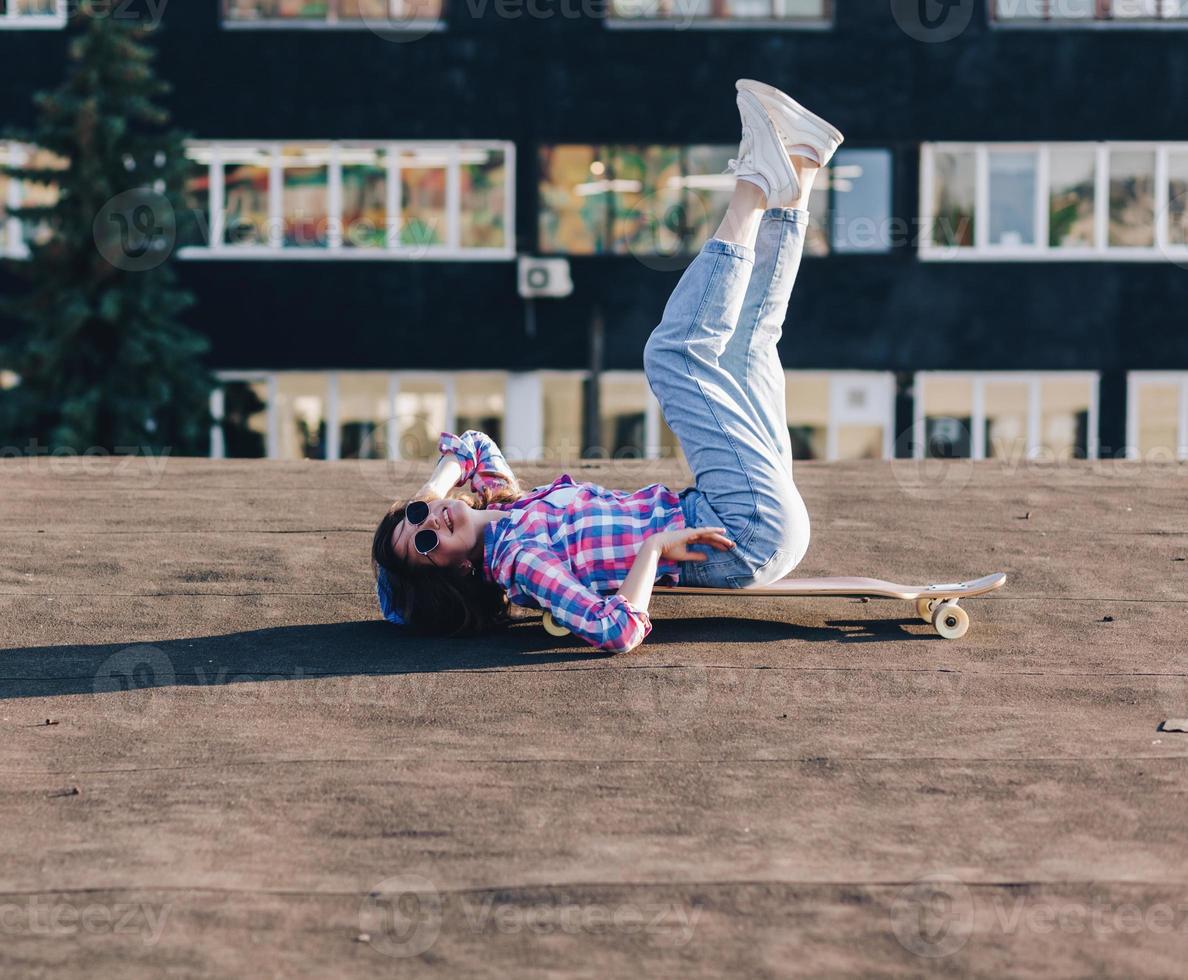 Teenager-Mädchen in stylischer Kleidung liegt auf einem Skateboard foto