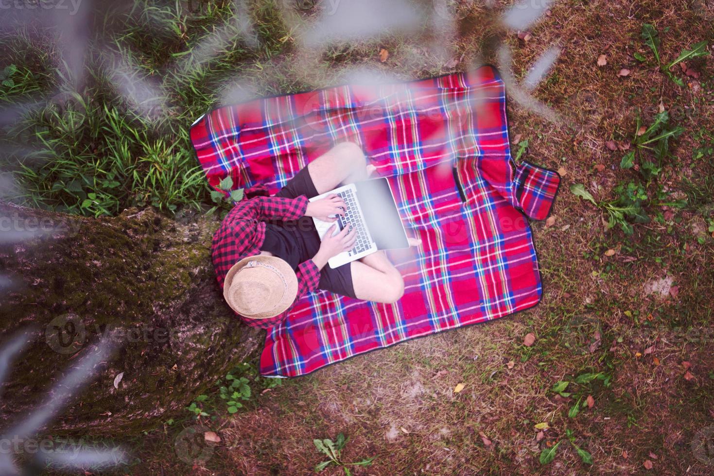 Draufsicht des Menschen mit einem Laptop-Computer unter dem Baum foto