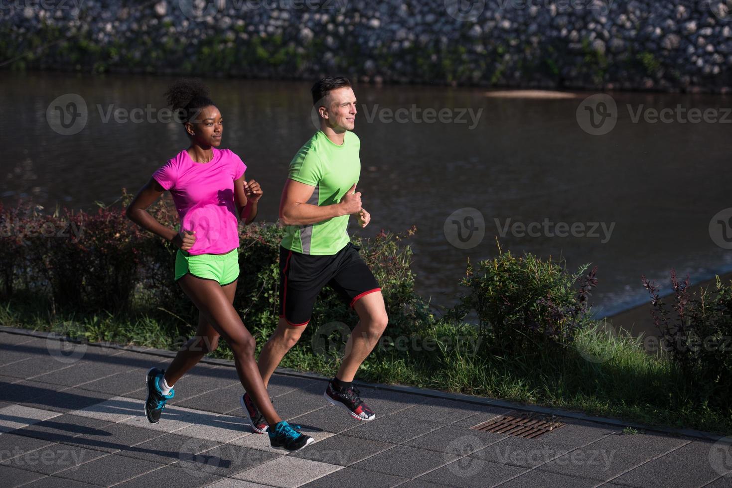 Junges lächelndes multiethnisches Paar, das in der Stadt joggt foto