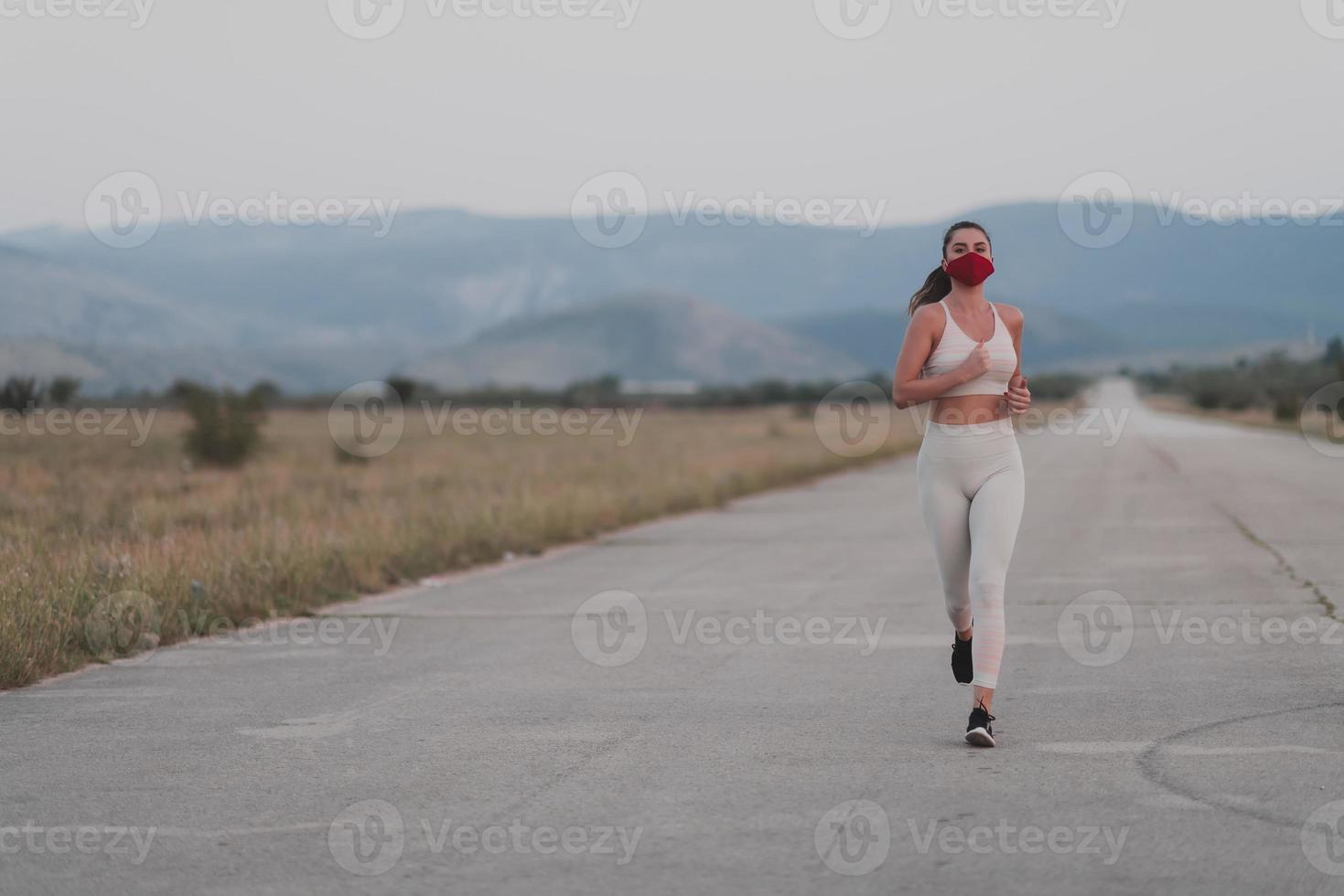 entschlossene fitnessfrau in kurzen kleidern mit roter gesichtsschutzmaske, die während des ausbruchs des coronavirus im freien in der stadt läuft. covid 19 und körperliche joggingaktivität sport und fitness. foto