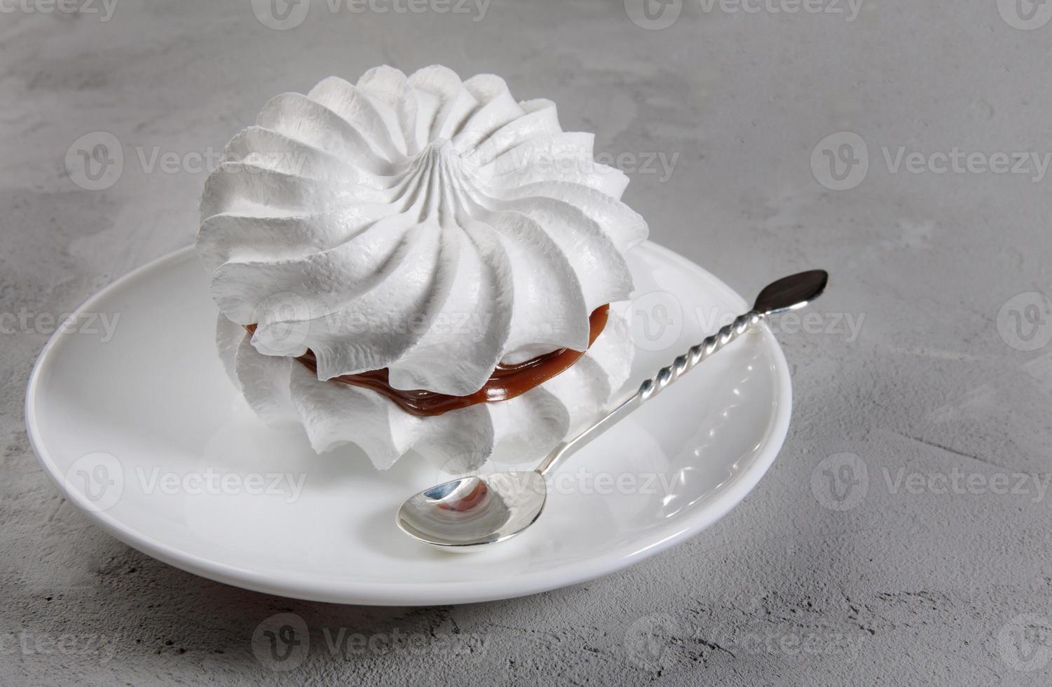 schöne weiße Baisers mit einem silbernen Löffel auf einem weißen Teller. weißer Kuchen. foto
