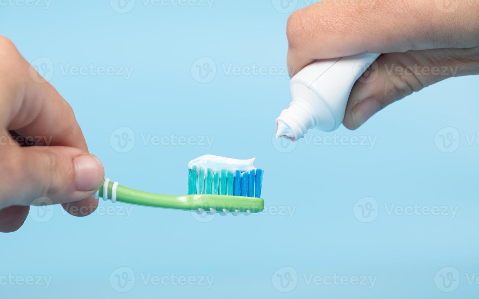 zahnpasta wird auf die zahnbürste aufgetragen, zahnputzen in der hand auf blauem hintergrund foto