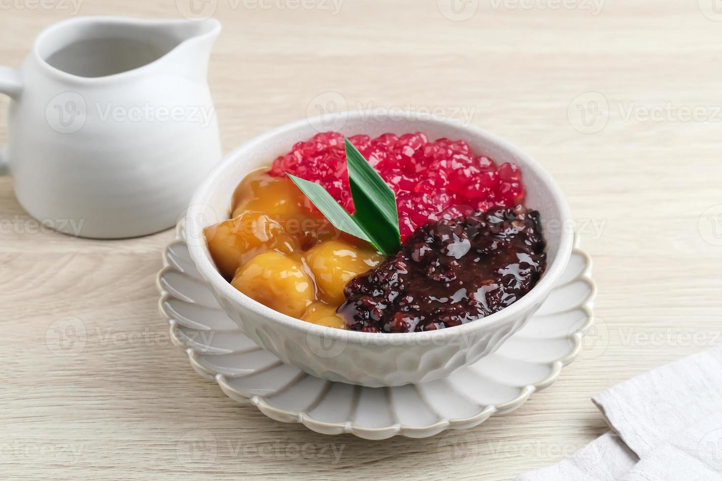 Bubur Madura, traditionelles indonesisches Dessert. schwarzer Klebreis mit Candil und Sagu Mutiara Brei und Pandanblatt. serviert in weißer schüssel auf holztisch. selektiver Fokus. foto